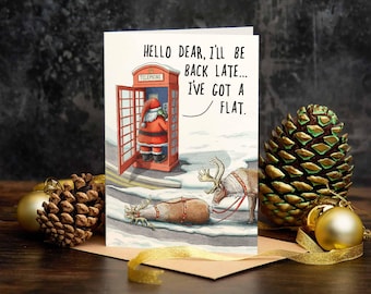 以下が含まれることがあります： 赤い電話ボックスにサンタクロースが描かれたクリスマスカード。「Hello Dear, I'll be back late... I've got a flat.」というテキスト。タイヤがパンクしたそりを引くトナカイ。背景には金のオーナメントと松ぼっくりがあります。