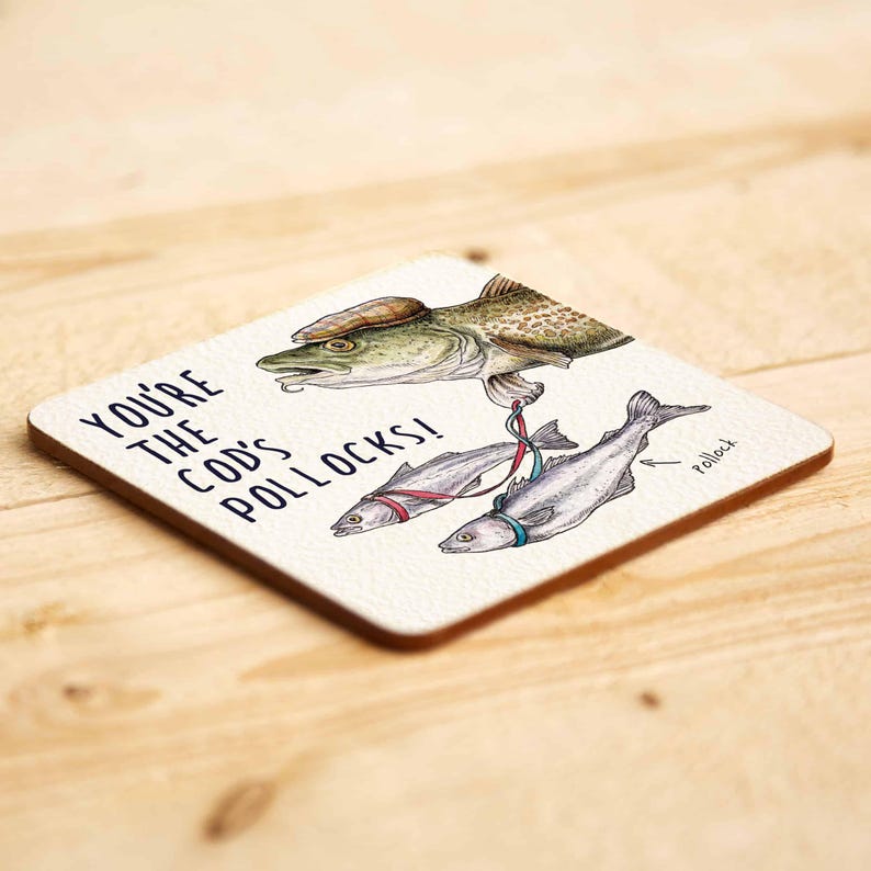 May include: A white coaster featuring a humorous illustration of a cod fish holding two smaller fish on leashes. The text on the coaster reads "You're the cod's pollocks!"