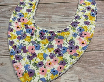 May include: A white bib with a floral pattern featuring pink, purple, and blue flowers. The bib has a soft, terrycloth lining.