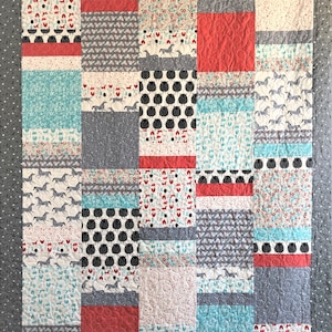 May include: A patchwork quilt with a variety of patterns in shades of gray, white, red, and blue. The quilt is made up of squares and rectangles, and the patterns include floral prints, animal prints, and geometric designs.