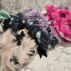 May include: A selection of fluffy accessories in pink, purple, black, and light peach. The items have a plush texture and feature accents of black and mint green. The accessories appear to be part of a costume or cosplay set.