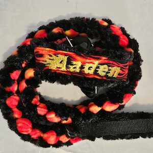 May include: Black and red dog leash with a fluffy texture and a black strap. The leash has a gold embroidered name "Jaden" on it.