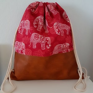 May include: A red drawstring bag with a white elephant print and a brown leather bottom. The bag has white drawstrings.