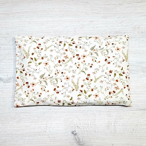 May include: A white pillow with a floral pattern in shades of brown, pink, and green. The pillow is made of fabric and has a rectangular shape.