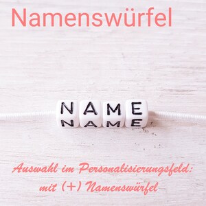 May include: White plastic beads spelling out the word "NAME" on a white string. The text "Auswahl im Personalisierungsfeld: mit (+) Namensw&uuml;rfel" is written in pink below the beads.