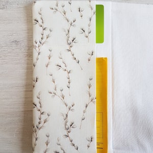 May include: A white fabric envelope with a floral pattern featuring small grey branches and buds. The envelope has a yellow pocket on the right side and a green pocket on the left side.
