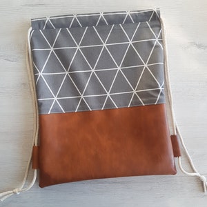 Peut inclure: Un sac à cordon de couleur gris et blanc à motif géométrique avec un fond en simili cuir marron.