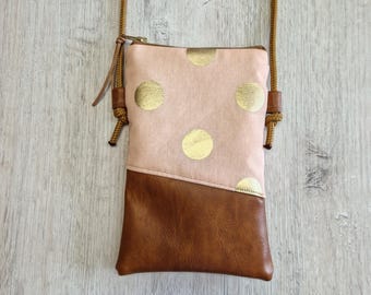 May include: A small, rectangular crossbody bag with a light pink upper section featuring gold polka dots. The lower section is brown leather. The bag has a brown cord strap and a gold zipper.