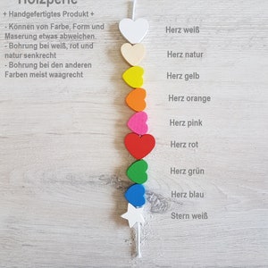 May include: A string of wooden heart-shaped beads in various colours, including white, natural, yellow, orange, pink, red, green, and blue. The beads are strung on a white cord and are arranged in a vertical line. The last bead is a white star. The text "Holzperle" is visible at the top of the image.