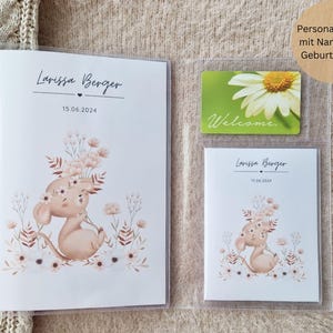 Può includere: Un album fotografico bianco con una copertina in plastica trasparente. L'album presenta una simpatica illustrazione di un topo marrone con fiori rosa. L'album è personalizzato con il nome "Larissa Berger" e la data "15.06.2024".