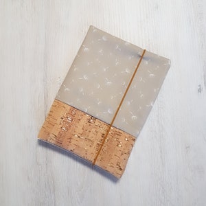 Könnte beinhalten: Eine beige Stofftasche mit Korkboden und einem weißen Löwenzahnmuster. Die Tasche hat einen braunen Gummizugverschluss.