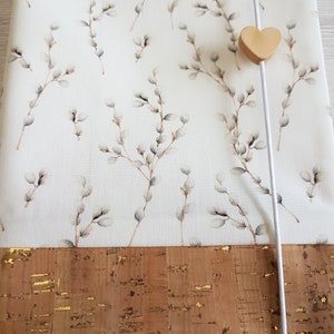May include: A white fabric notebook cover with a delicate willow branch pattern. The cover has a brown cork bottom with gold flecks and a white ribbon closure with a wooden heart charm.