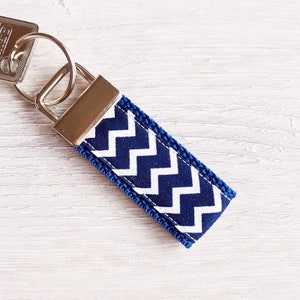 Könnte beinhalten: Ein Schlüsselanhänger mit Chevron-Muster in Marineblau und Weiß mit einem silbernen Schlüsselring.