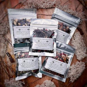 May include: Five small silver pouches containing loose leaf tea blends. Each pouch has a label with a name and ingredients. The names are "Mind Flayers Contract", "Vampire Lord's Spawn", "Driders Hunt", "The Harpy's Ballad", and "A Cambion's Desire".