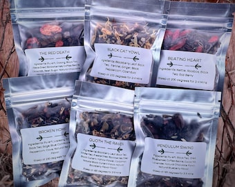 May include: Six small clear plastic bags filled with loose leaf tea blends. Each bag has a white label with a black border and a name for the tea blend. The names are "The Red Death", "Black Cat Yowl", "Beating Heart", "Broken Home", "Quoth the Raven", and "Pendulum Swing".