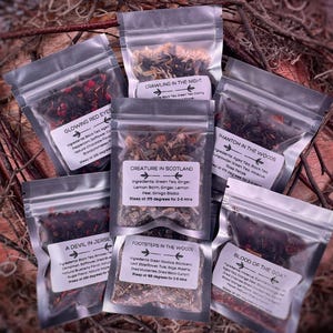 May include: Assortment of small, clear plastic bags filled with loose leaf tea blends. Each bag has a label with a unique name and ingredients list. The names include "Glowing Red Eyes", "Crawling in the Night", "Creature in Scotland", "Phantom in the Woods", "A Devil in Jersey", "Footsteps in the Woods", and "Blood of the Goat".
