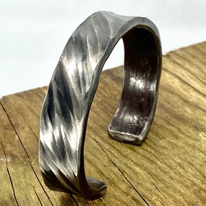 May include: A silver metal bracelet with a textured, twisted design. The bracelet is open and has a slightly rounded shape.
