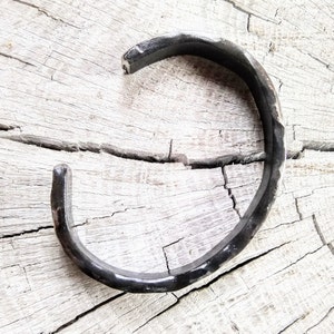 May include: A simple, black metal bracelet with a hammered finish. The bracelet is open and has a slightly curved shape.