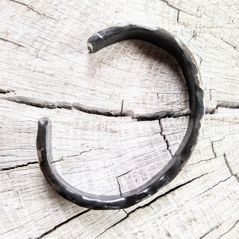 May include: A simple, black metal bracelet with a hammered finish. The bracelet is open and has a slightly curved shape.