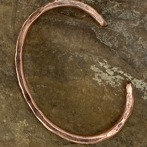 K&ouml;nnte beinhalten: Ein geh&auml;mmertes Kupferarmband mit glatter, abgerundeter Oberfl&auml;che. Das Armband ist offen und bereit zum Tragen.