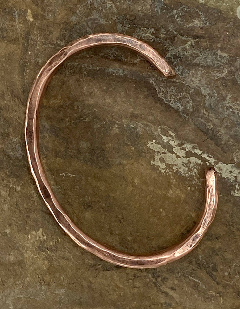 K&ouml;nnte beinhalten: Ein geh&auml;mmertes Kupferarmband mit glatter, abgerundeter Oberfl&auml;che. Das Armband ist offen und bereit zum Tragen.