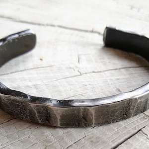 May include: A silver metal bracelet with a hammered finish. The bracelet is open and has a slightly curved shape.