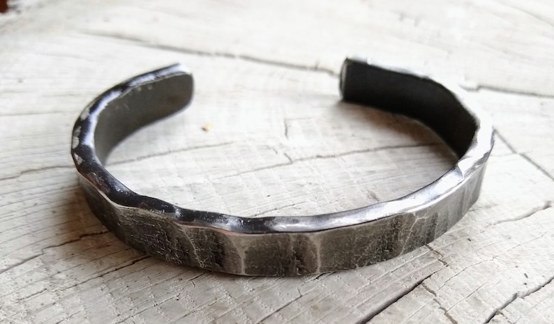 May include: A silver metal bracelet with a hammered finish. The bracelet is open and has a slightly curved shape.