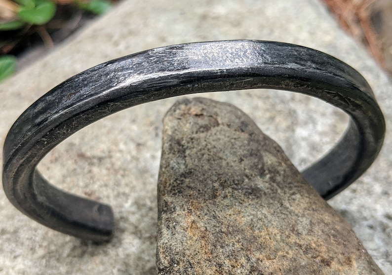 Puede incluir: Un brazalete de metal negro con acabado martillado. El brazalete est&aacute; hecho de un metal grueso y resistente y tiene un dise&ntilde;o simple y minimalista.