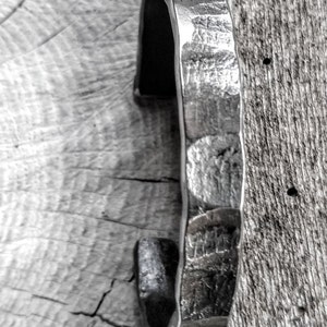 May include: A silver metal bracelet with a hammered texture. The bracelet is open and has a slightly curved shape.
