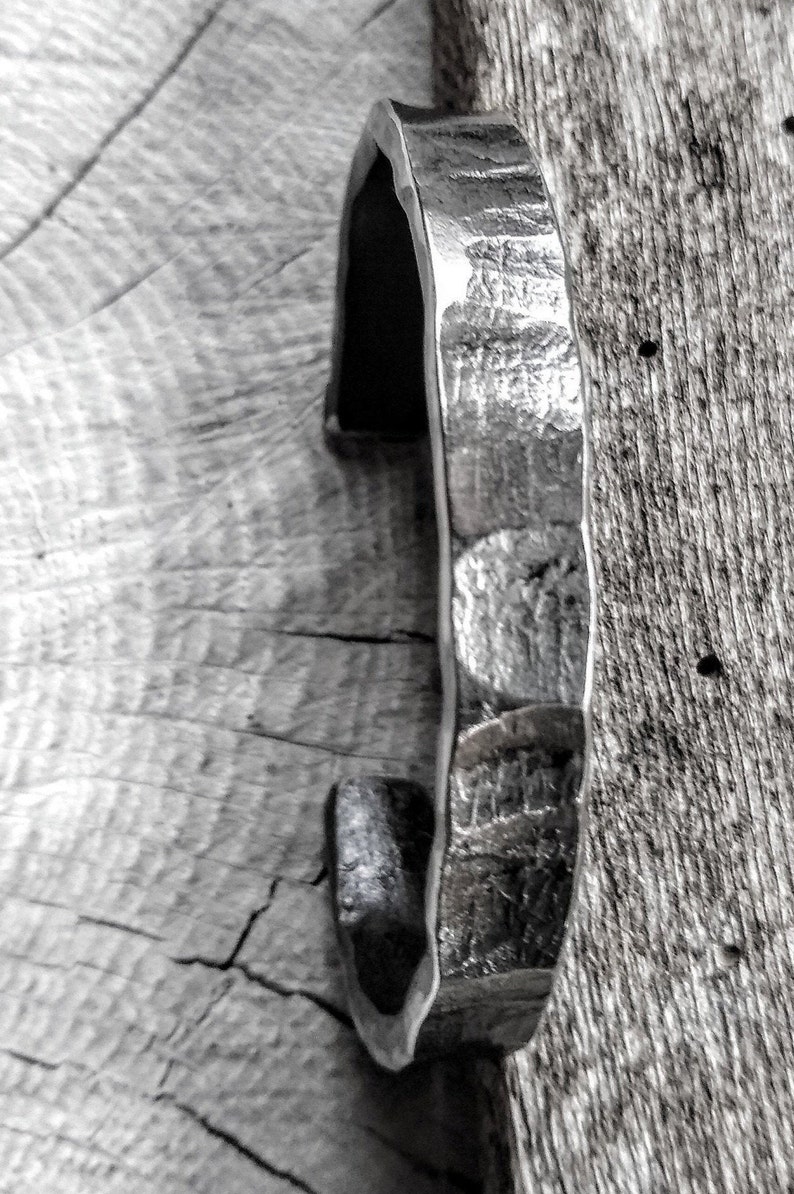May include: A silver metal bracelet with a hammered texture. The bracelet is open and has a slightly curved shape.