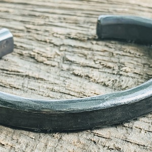 Puede incluir: Una pulsera de metal simple, de color plateado, con una superficie redondeada ligeramente texturizada.