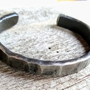 May include: A silver metal bracelet with a hammered texture. The bracelet is open and has a simple design.