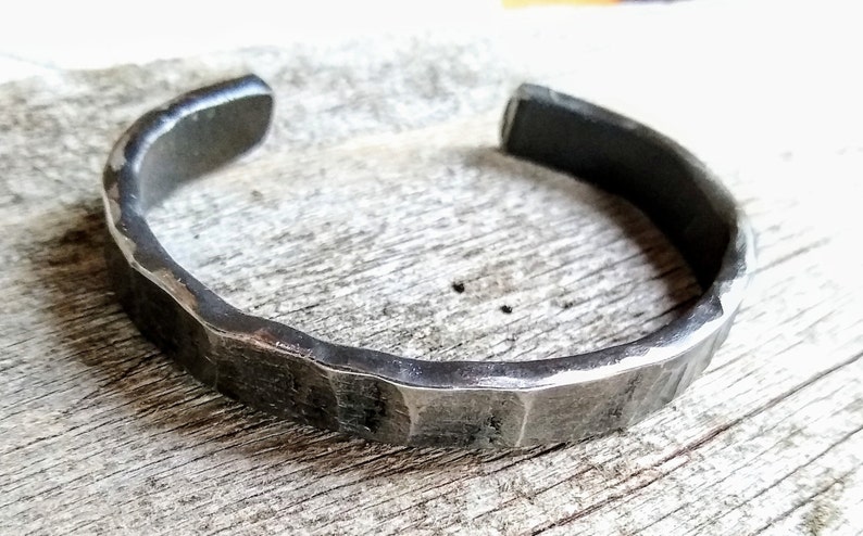 May include: A silver metal bracelet with a hammered texture. The bracelet is open and has a simple design.