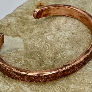 K&ouml;nnte beinhalten: Ein geh&auml;mmertes Kupferarmband mit rustikalem Finish. Das Armband ist offen und hat ein schlichtes Design.