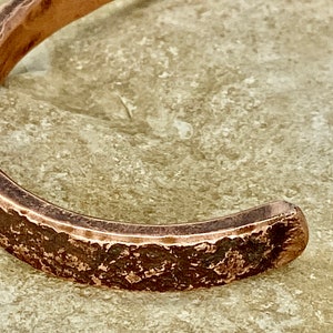 K&ouml;nnte beinhalten: Nahaufnahme eines Kupferarmbands mit geh&auml;mmerter Textur. Das Armband ist offen und hat eine leicht abgerundete Form.