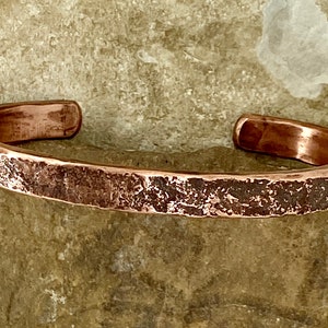 K&ouml;nnte beinhalten: Ein geh&auml;mmertes Kupferarmband mit rustikalem Finish. Das Armband besteht aus einem einzigen St&uuml;ck Kupfer, das geh&auml;mmert und strukturiert wurde, um ein einzigartiges und auff&auml;lliges Design zu schaffen.