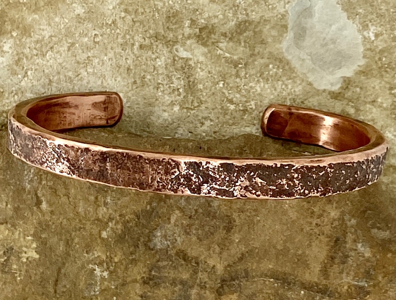 K&ouml;nnte beinhalten: Ein geh&auml;mmertes Kupferarmband mit rustikalem Finish. Das Armband besteht aus einem einzigen St&uuml;ck Kupfer, das geh&auml;mmert und strukturiert wurde, um ein einzigartiges und auff&auml;lliges Design zu schaffen.