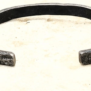 May include: A silver metal bracelet with a hammered texture. The bracelet is open and has a simple design.