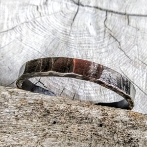 May include: A silver hammered metal bracelet with a slightly rounded shape.