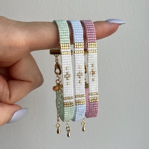 Könnte beinhalten: Drei Perlenarmbänder in Pastellgrün, Hellblau und Rosa mit goldenen Akzenten. Die Armbänder haben ein schlichtes geometrisches Design und sind auf einer goldenen Kette mit einem Verschluss aufgefädelt.