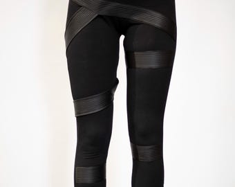 May include: Black leggings featuring horizontal ribbed elastic bands wrapped around the thighs, knees, and calves. The leggings have a high-waisted fit and are paired with black high-top sneakers with a smooth finish and white soles.