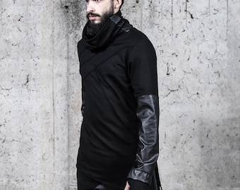 Puede incluir: Una camiseta negra de manga larga con cuello alto tipo chimenea, costuras diagonales en el pecho y mangas de cuero sintético texturizado en contraste. La prenda tiene un dobladillo largo e incluye aberturas para los pulgares.