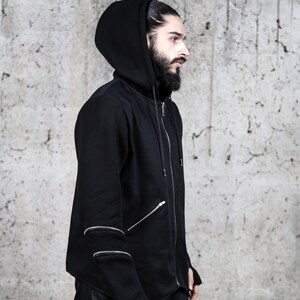 May include: A black hooded sweatshirt with a zip fastening and multiple zipper details on the sleeves. The sweatshirt has a relaxed fit and a long, asymmetrical hem.