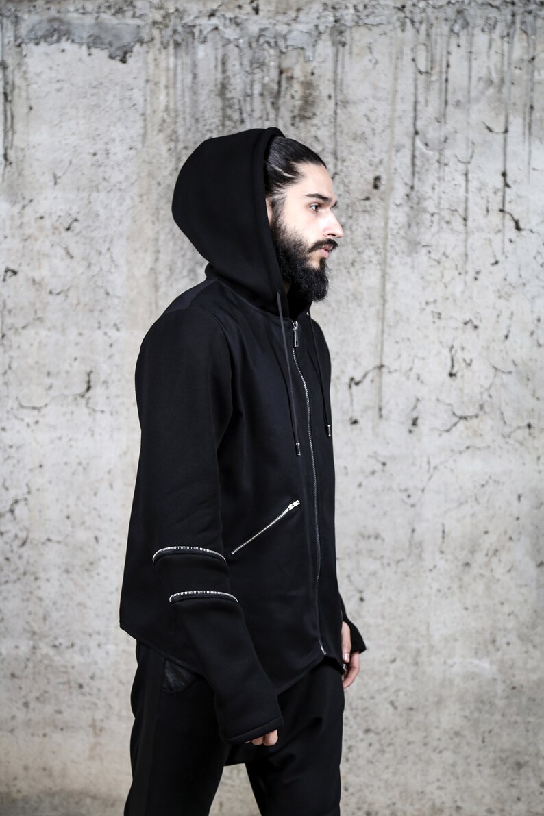May include: A black hooded sweatshirt with a zip fastening and multiple zipper details on the sleeves. The sweatshirt has a relaxed fit and a long, asymmetrical hem.