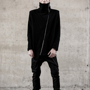 May include: A person wearing a black outfit with a high collar and a diagonal zipper. The outfit includes a long-sleeved top and matching pants. The person is also wearing black boots. The background is a concrete wall.