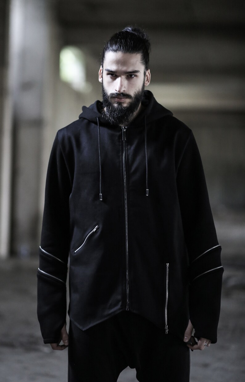 May include: A black zip-up hoodie with silver zipper accents and a drawstring hood. The hoodie has a long, asymmetrical hemline and a relaxed fit.