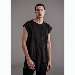Może przedstawiać: Czarna koszulka bez rękawów z unikalnym asymetrycznym wzorem. Koszulka ma luźny krój i nieco dłuższy fason.