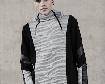 Puede incluir: Una sudadera con capucha gris y negra con cuello alto y un patrón texturizado en forma de ola en la parte delantera. Las mangas y los laterales son negros con detalles de cuero. La cremallera recorre la parte delantera.