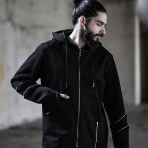 May include: A black zip-up hoodie with a long, pointed hem and silver zipper accents. The hoodie has a drawstring hood and long sleeves with silver accents on the cuffs.