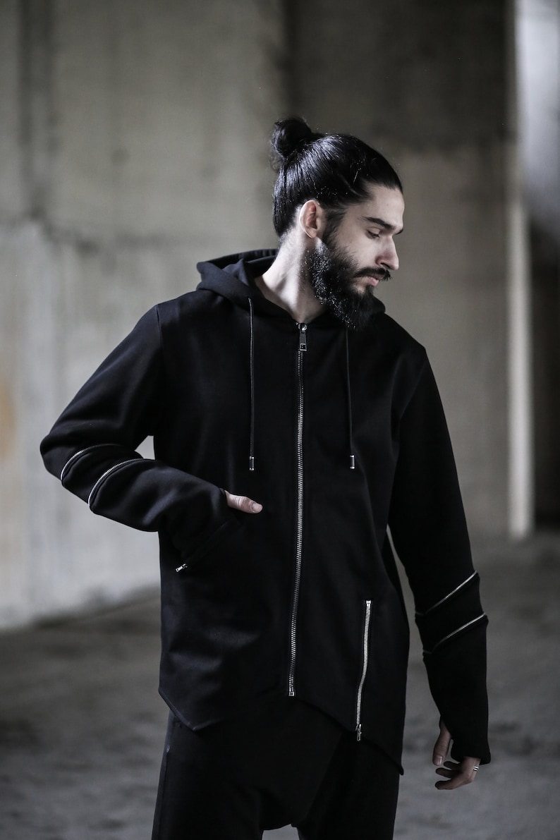 May include: A black zip-up hoodie with a long, pointed hem and silver zipper accents. The hoodie has a drawstring hood and long sleeves with silver accents on the cuffs.